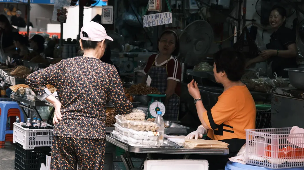 Người bán ở sạp chợ cân hàng cho khách, minh họa so sánh thuế hộ kinh doanh và công ty